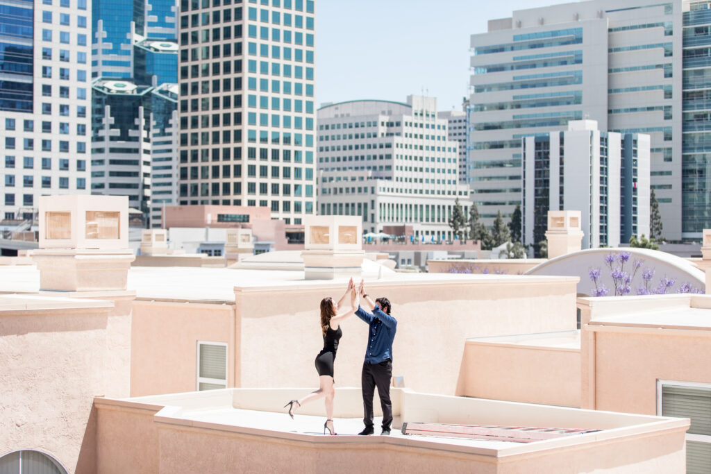 Newly engaged couple standing on a roof top in San Diego posing for engagement photos taken by luxury destination wedding photographer Julie Ferneau