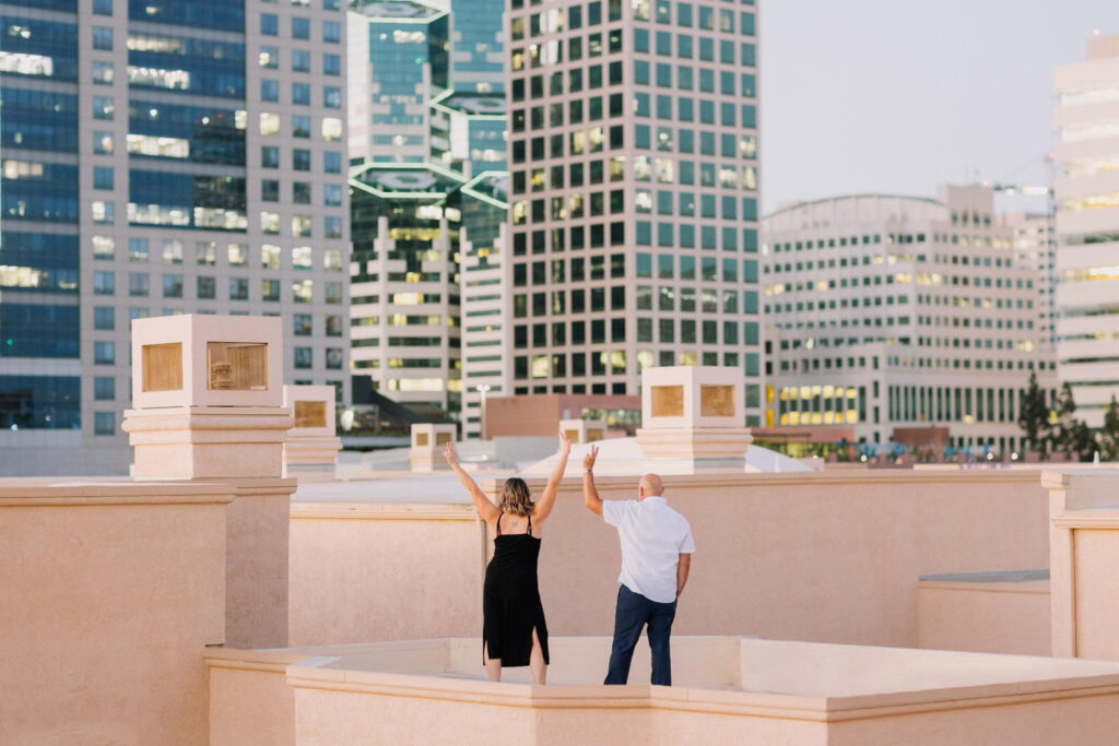 Photo of a couple standing on the rooftop of a Downtown San Diego building with peace signs