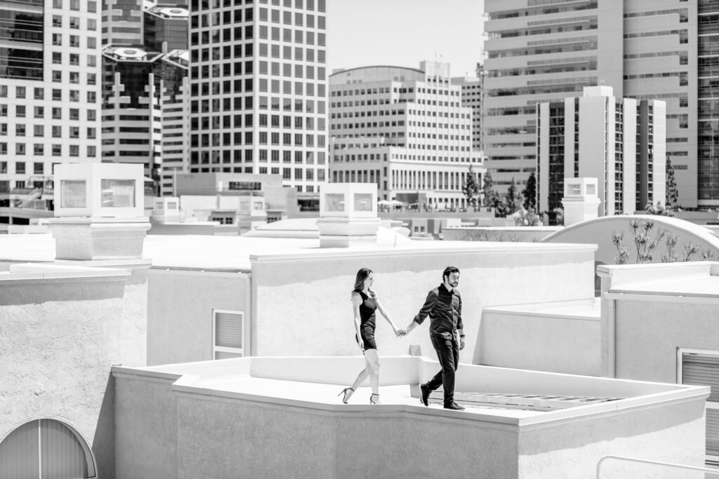 Newly engaged couple standing on a roof top in San Diego posing for engagement photos taken by luxury destination wedding photographer Julie Ferneau